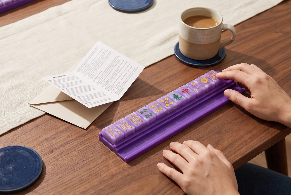 A new mahjong card on its envelope beside a row of purple tiles and a cup of coffee
