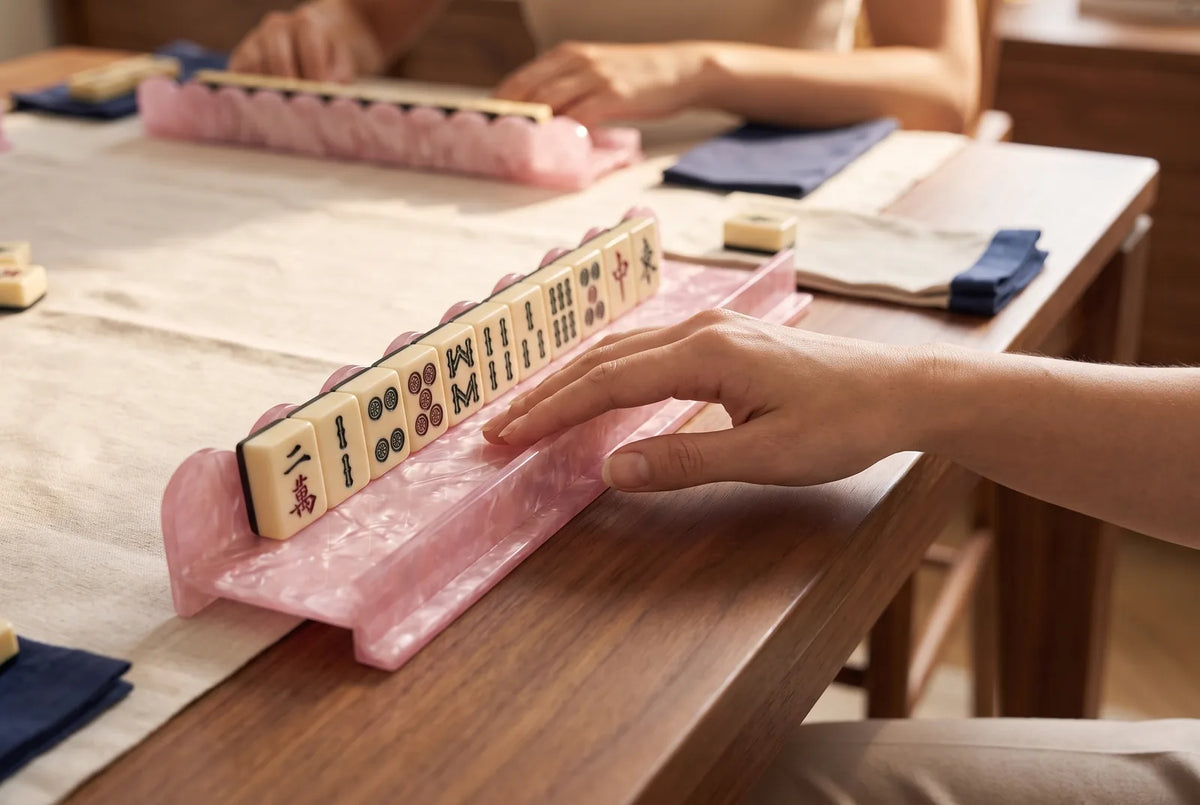 A hand slides a wall of tiles forward with the pusher arm of a pink mahjong rack