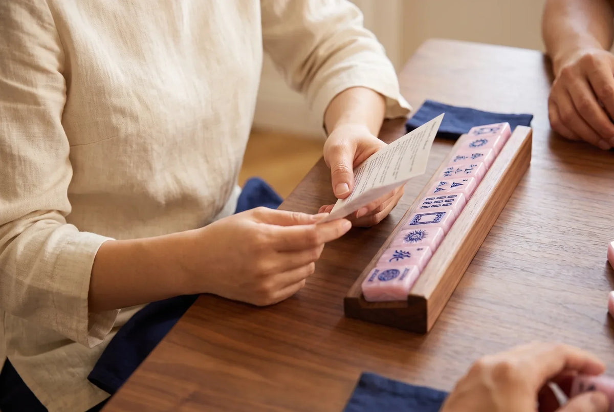 A player holds a small mahjong card beside her rack of purple tiles