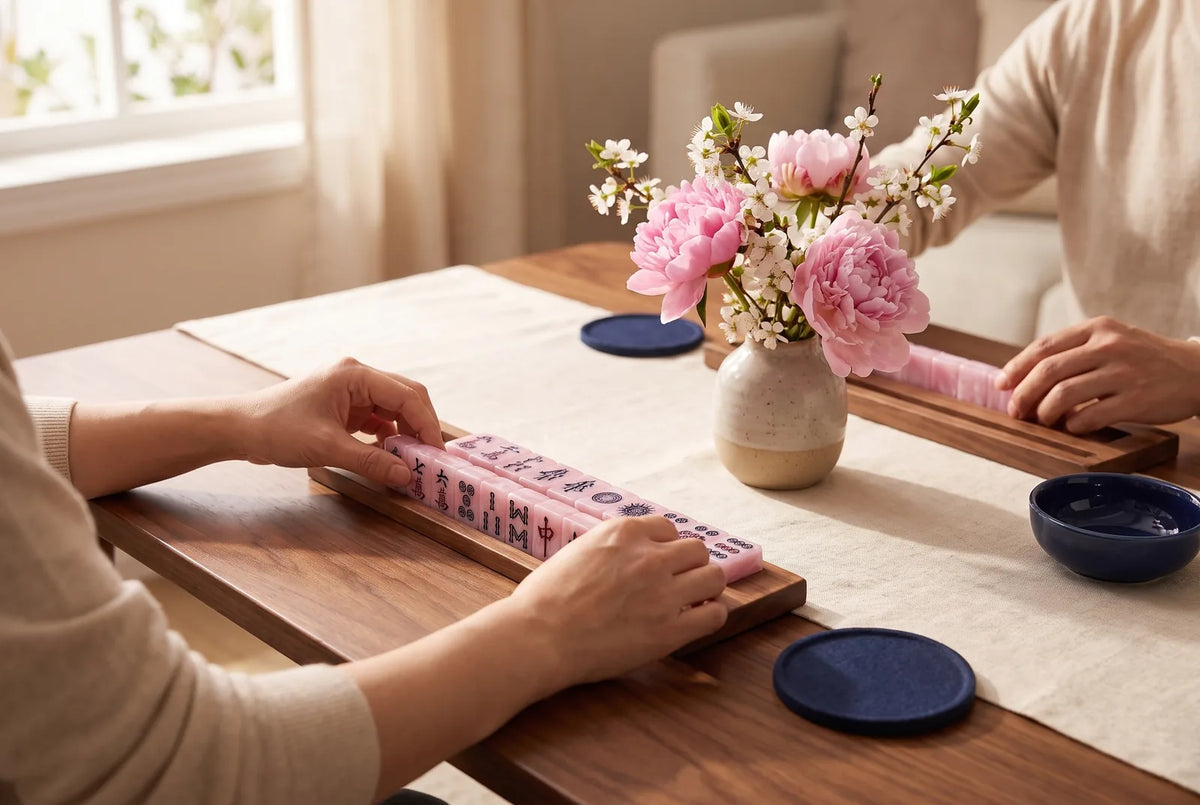 Mahjong tiles on a rack beside a small vase of fresh pink flowers